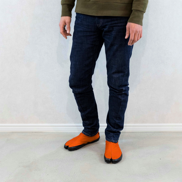 Person wearing orange Tabi Shoes "U-ten" in a casual standing pose indoors