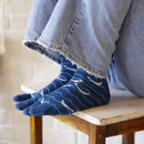 Close-up of blue Shirasu tabi socks featuring a split-toe design with white patterns, shown worn with denim pants.
