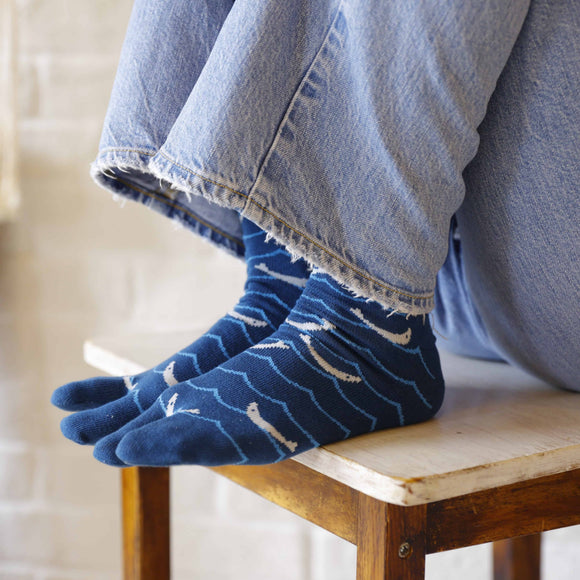 Close-up of blue Shirasu tabi socks featuring a split-toe design with white patterns, shown worn with denim pants.