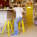 Lifestyle image of a woman wearing MARU SANKAKU SHIKAKU tabi socks while sitting on a yellow stool in a bright, playful interior.
